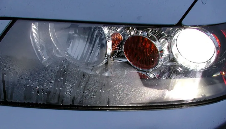 Farol automotivo com gotas de água e condensação acumulada internamente, mostrando umidade na lente transparente