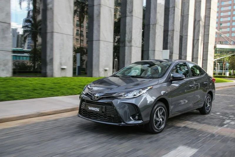 Toyota Yaris Sedã cinza-chumbo em movimento com rodas de liga leve, faróis de LED e logotipo Yaris no para-choque