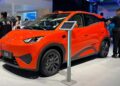 Carro elétrico BYD Seagull laranja em estande de exposição, com visitantes ao redor e totem informativo