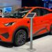 Carro elétrico BYD Seagull laranja em estande de exposição, com visitantes ao redor e totem informativo