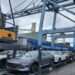 Carros elétricos cinza e branco sobre plataforma no porto, guindaste Login, navio Cosco Shipping ao fundo