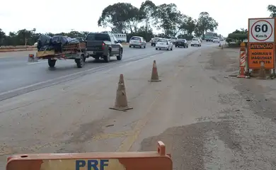 Carros passando por fiscalização na estrada, cones laranja, placa da PRF e limite 60 km/h