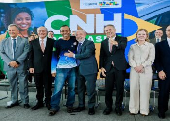 Grupo de autoridades e motorista sorridente em frente ao painel da CNH, ministro e presidente ao centro, ambiente institucional
