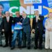 Grupo de autoridades e motorista sorridente em frente ao painel da CNH, ministro e presidente ao centro, ambiente institucional