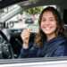 Adolescente sorrindo dentro do carro segura CNH brasileira em destaque, usando moletom azul