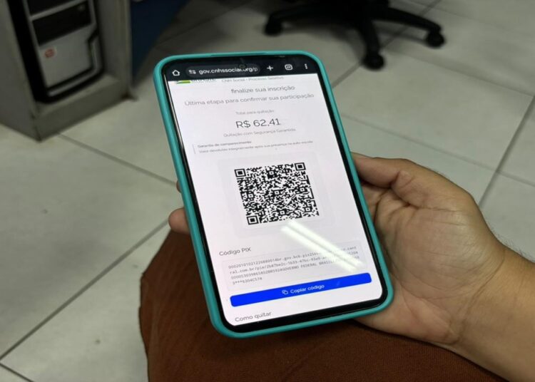 Pessoa segurando celular mostrando site falso da CNH Social com QR Code e valor R$ 62,41