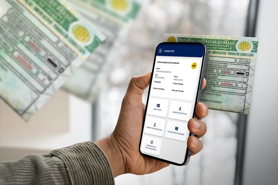 Mão masculina segura celular mostrando aplicativo da CNH digital próximo à carteira de motorista impressa, fundo desfocado