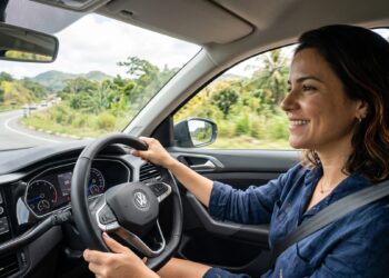 Mulher jovem dirigindo carro Volkswagen em estrada com vegetação e montanhas ao fundo