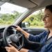 Mulher jovem dirigindo carro Volkswagen em estrada com vegetação e montanhas ao fundo