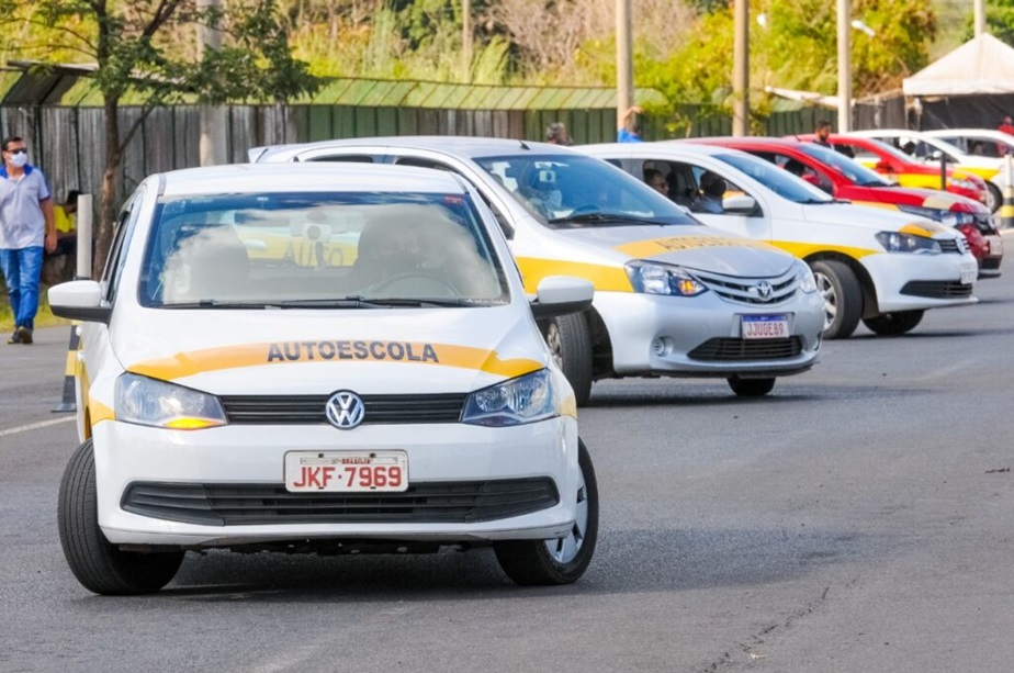 Veículos de autoescola brancos e amarelos em fila numa via, com destaque para Volkswagen placa JKF-7969