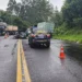Viatura da PRF com cones laranjas em rodovia molhada de pista simples, caminhões e carro acidentado ao fundo