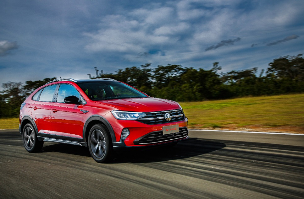 Volkswagen Nivus vermelho trafegando em pista sob céu azul com árvores ao fundo