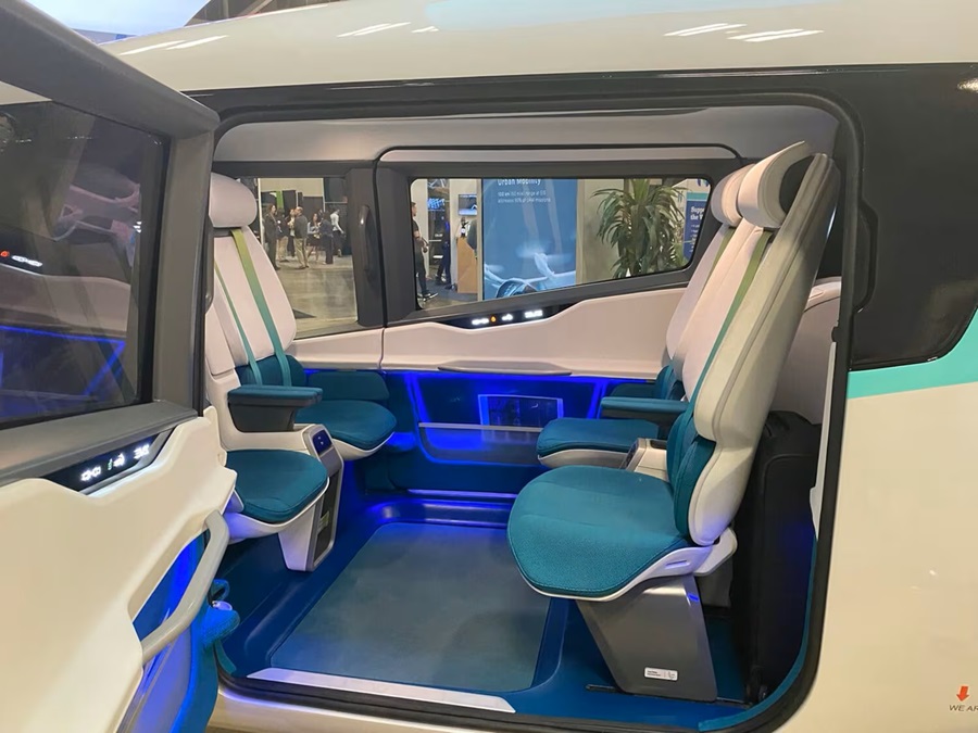 Interior do eVTOL Eve 100 com 4 assentos em azul turquesa, cintos verdes, iluminação LED azul e janelas amplas em exposição