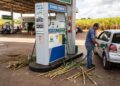 Frentista abastece Volkswagen Gol prata com etanol em posto BR Petrobras, canas-de-açúcar ao redor da bomba