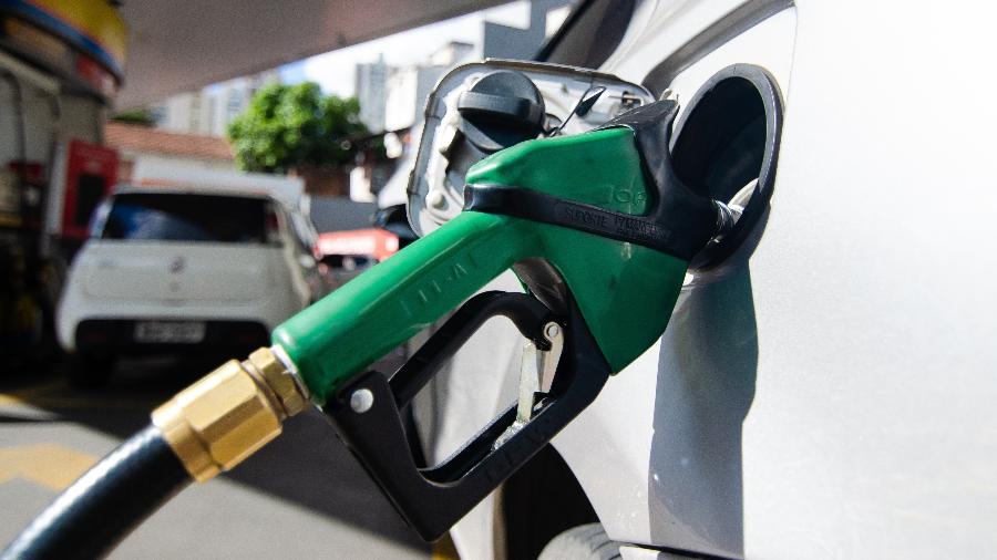 Bico de bomba de combustível verde inserido no tanque de carro branco durante abastecimento em posto