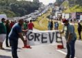 Caminhoneiros seguram faixa com a palavra “GREVE”, bloqueando rodovia cheia de caminhões parados