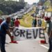 Caminhoneiros seguram faixa com a palavra “GREVE”, bloqueando rodovia cheia de caminhões parados
