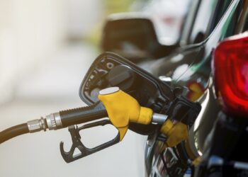 Bomba de combustível amarela e preta inserida no tanque de carro escuro em posto de gasolina, durante prorrogação de subsídio.