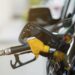 Bomba de combustível amarela e preta inserida no tanque de carro escuro em posto de gasolina, durante prorrogação de subsídio.