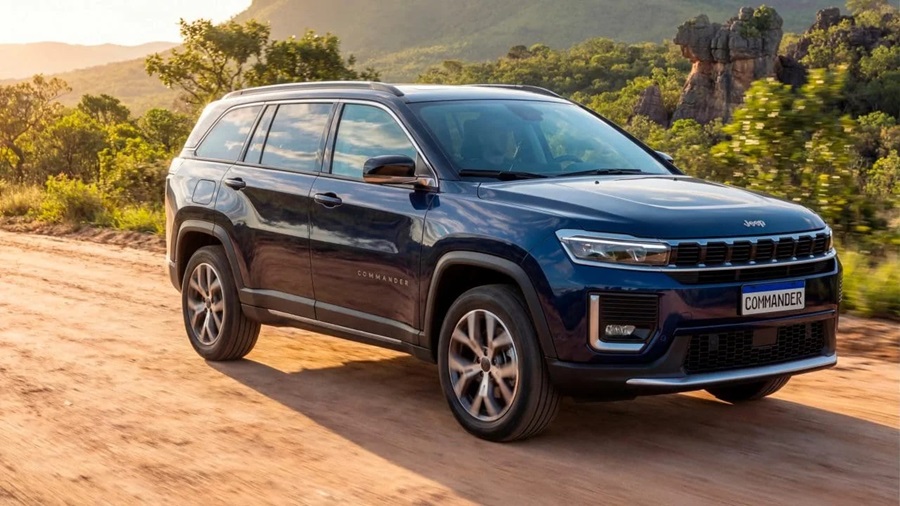 Jeep Commander azul-marinho com rodas de liga leve trafegando em estrada de terra com vegetação e montanhas rochosas