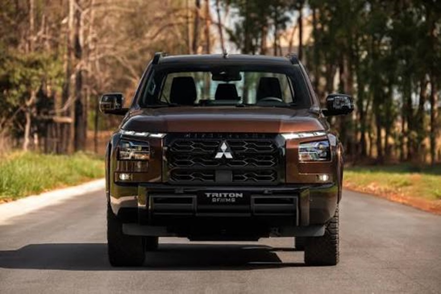 Mitsubishi Triton BF///MS na cor Marrom Barroco com grade preta, emblema central cromado e inscrição Triton em pista arborizada