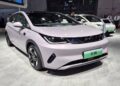 BYD Dolphin Mini branco em exposição, placas verdes e ambiente de salão automotivo chinês