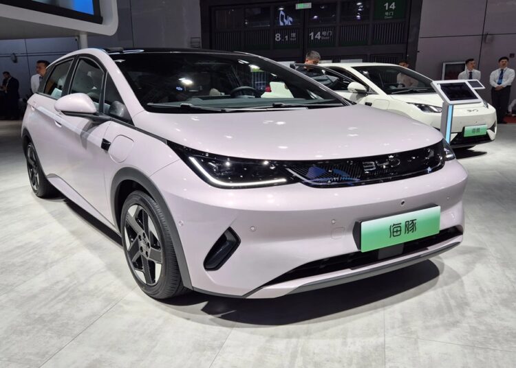 BYD Dolphin Mini branco em exposição, placas verdes e ambiente de salão automotivo chinês