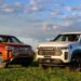 Duas picapes Ram Dakota 2026, uma laranja Laramie e outra branca Warlock, estacionadas em gramado verde sob céu azul