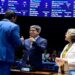 Três senadores interagem no plenário do Senado; homem ao centro faz sinal de positivo, ao lado de mulher de cabelos grisalhos, simbolizando a MP do frete.