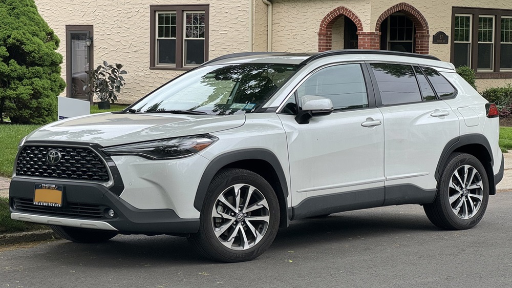 SUV Toyota Corolla Cross branco com teto preto estacionado em rua com casa de fundo bege ao fundo