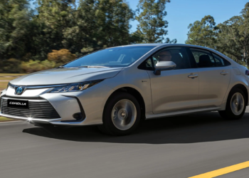 Toyota Corolla sedan prata trafega em rodovia com fundo de vegetação verde, exibindo grade frontal com emblema da marca