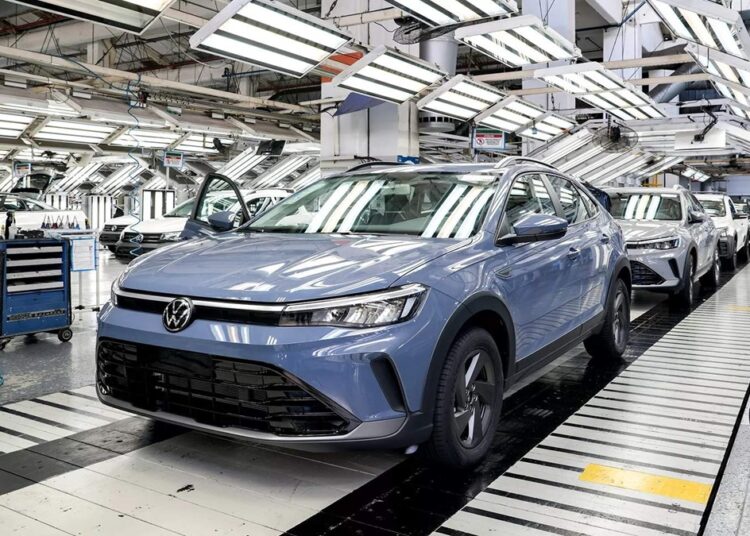 Nivus azul em destaque na linha de produção da Volkswagen, com outros veículos ao fundo sob iluminação industrial