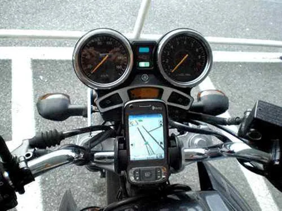Painel de motocicleta exibe velocímetro, conta-giros e celular com GPS rodando, visto de cima