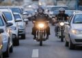 Dois motociclistas de capacete circulam entre carros parados no corredor de trânsito urbano
