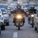 Dois motociclistas de capacete circulam entre carros parados no corredor de trânsito urbano