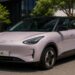 Representação do Geely EX2 Max ao lado de um carregador da marca, elétrico de R$ 136.800 que rodou 303 quilômetros no teste, superou os 289 km do Inmetro e recarrega de 30% a 80% em 21 minutos