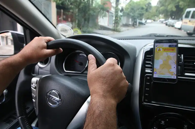 Homem dirige Nissan segurando volante com aplicativo Waze aberto no suporte do painel