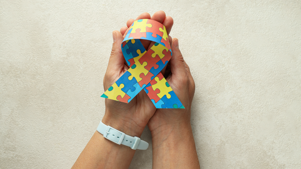Laço colorido do autismo destacado em mãos sobre fundo claro.