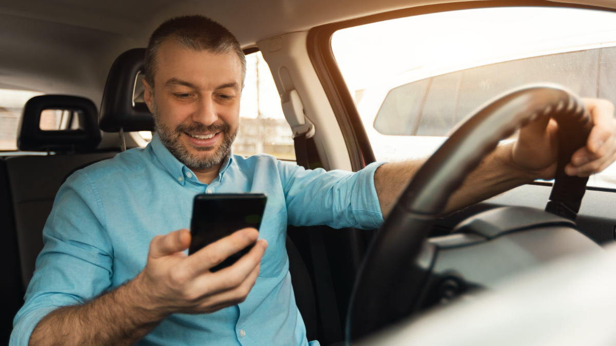 Motorista sorrindo ao usar celular.