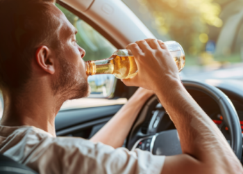 homem dirige carro e bebe cerveja.