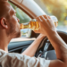 homem dirige carro e bebe cerveja.