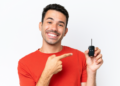 Homem sorridente destaca chave de carro moderna em fundo claro.