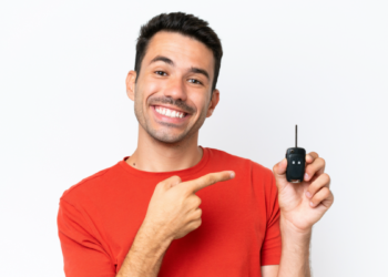 Homem sorridente destaca chave de carro moderna em fundo claro.