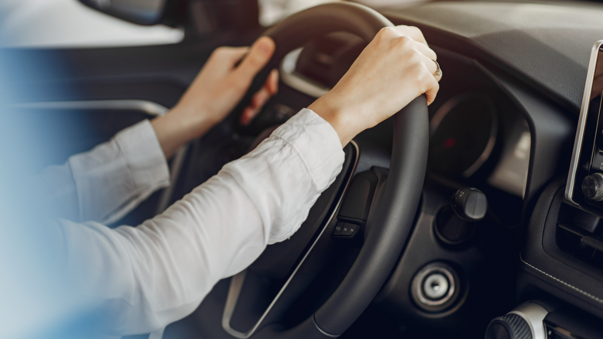 Mãos dirigindo carro moderno com camisa branca.
