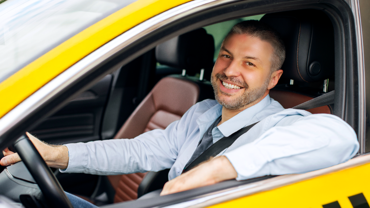 Motorista de táxi sorridente ao volante em ambiente urbano.