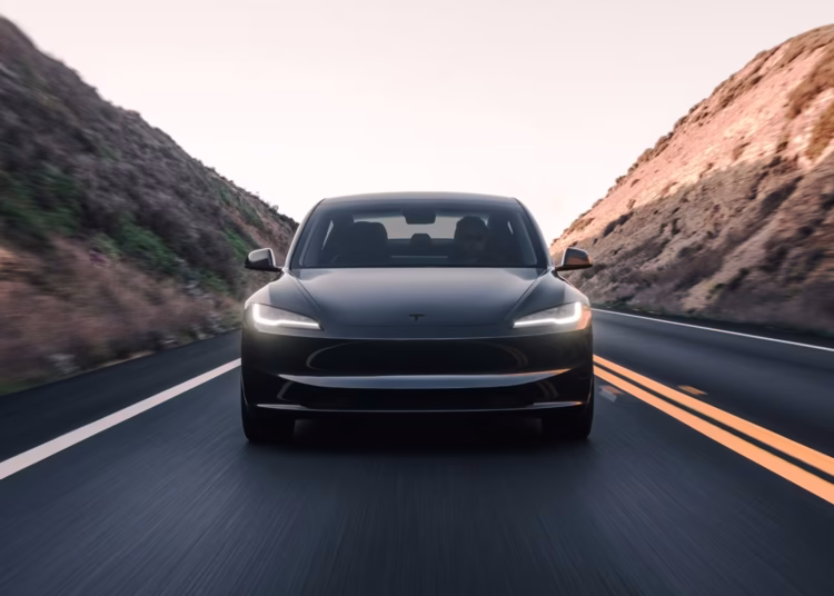 Carro Tesla modelo elétrico em rodovia cercada por montanhas.