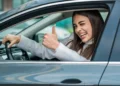 Mulher dentro de carro fazendo sinal de positivo com o polegar.