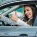 Mulher dentro de carro fazendo sinal de positivo com o polegar.