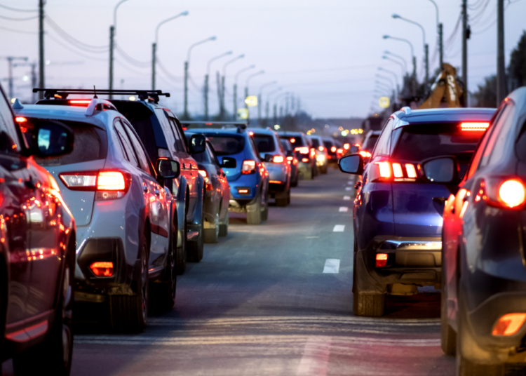 Engarrafamento em avenida urbana ao entardecer com carros parados.