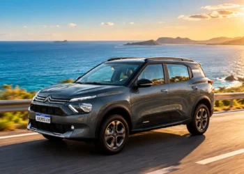 SUV cinza percorre uma estrada litorânea com o mar azul ao fundo, sob a luz intensa do sol.